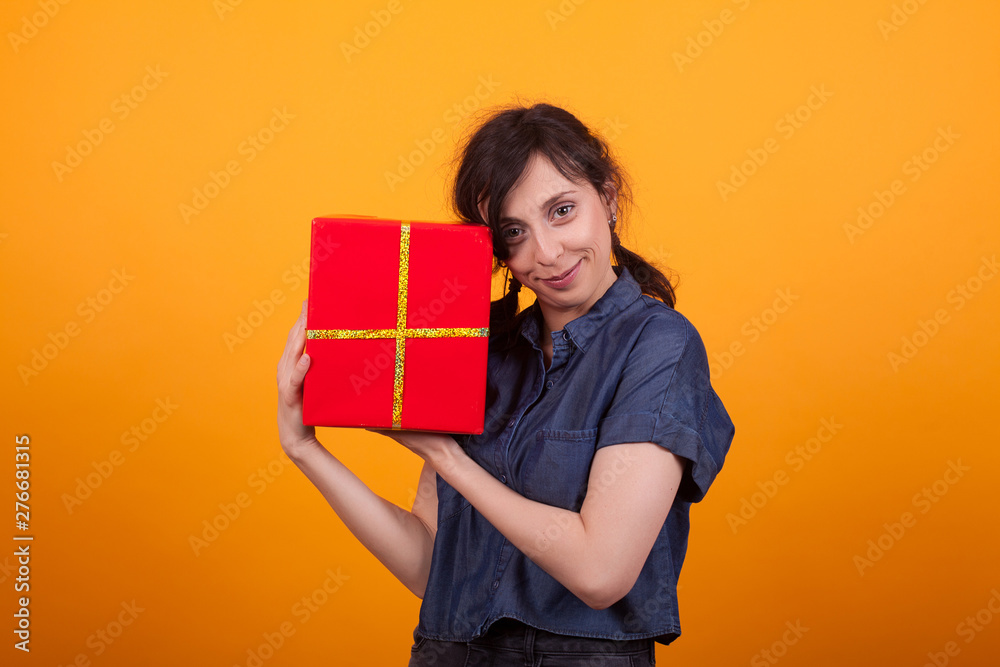 Portrait of happy young woman with her red gift box looking at the camera in studio over yellow background