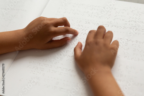 Blind schoolboy hands reading a braille book in classroom
