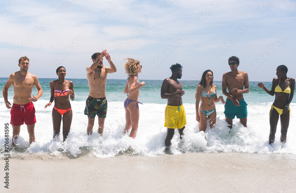 Group of friends relaxing  and standing in water at beach