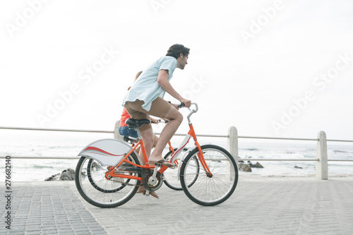 Caucasian couple riding bicycle on pavement near promenade at beach