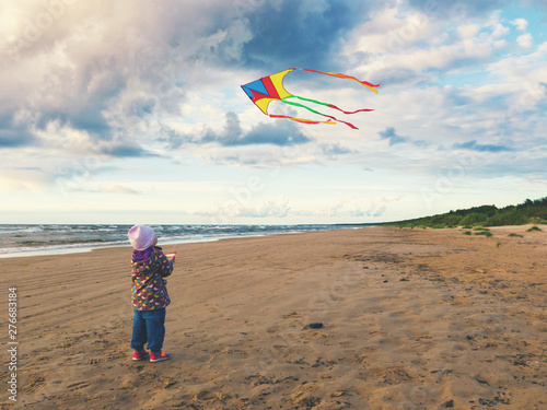 little girl flying a kite on the beach at sunset