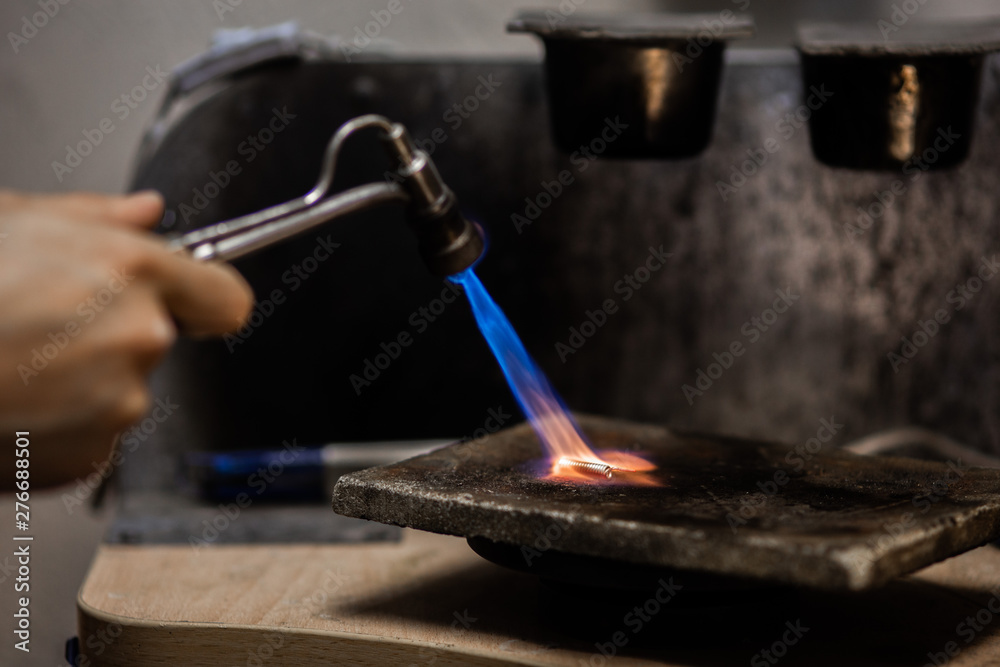 Craft jewelry with a torch flame against a dark background. Jeweler handles  metal rail by heating it.Beautiful bright close up photo. Stock Photo