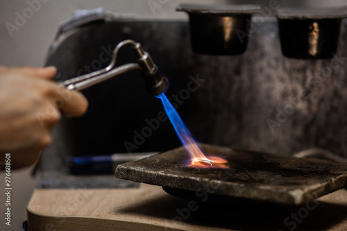 Craft jewelry with a torch flame against a dark background. Jeweler handles metal rail by heating it.Beautiful bright close up photo.