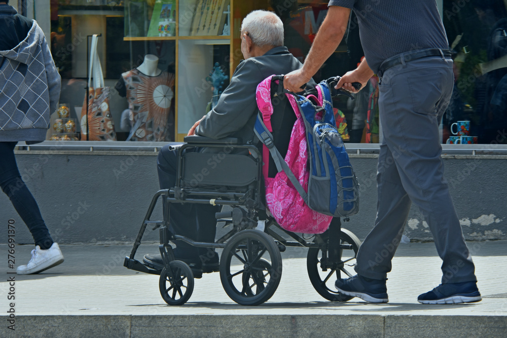 Obraz premium man carries an elderly person in a wheelchair, fragment