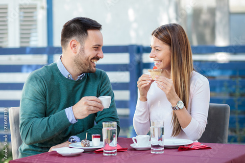 Beautiful happy young couple eating cakes and drinking coffee in a restaurant. Romantic date and anniversary celebration