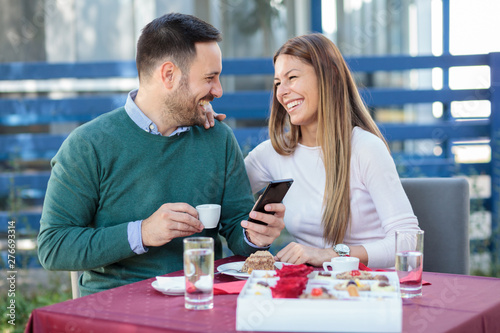 Smiling happy millennial couple celebrating anniversary or birthday in a restaurant. Eating cake and drinking coffee.