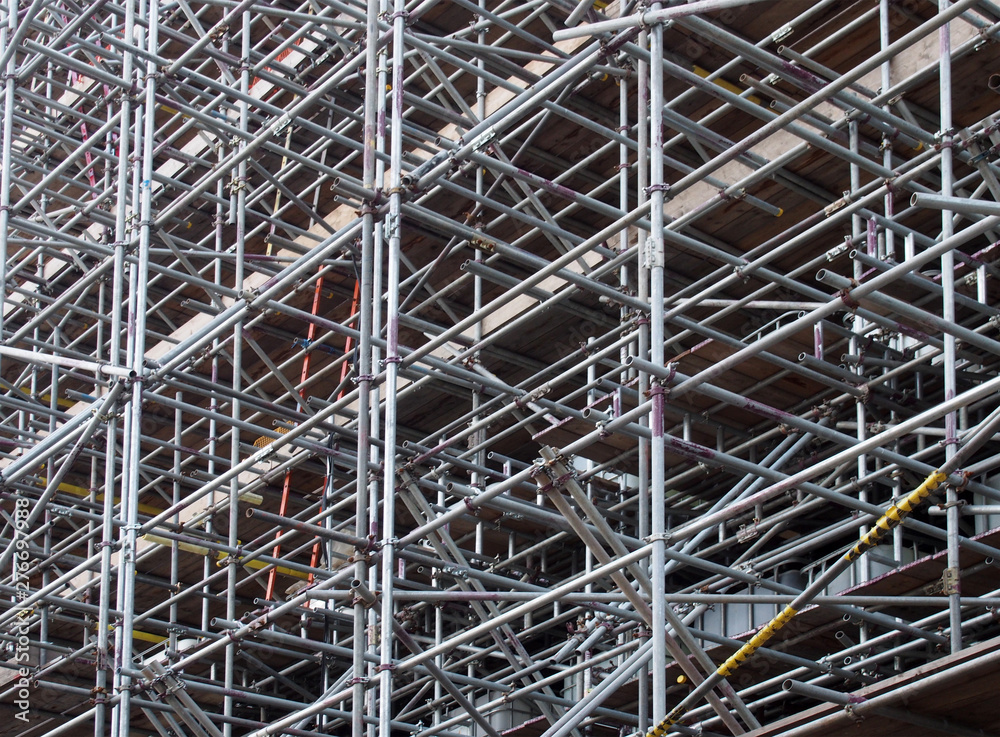 a dense network of metal scaffolding poles supporting work platforms on a construction site
