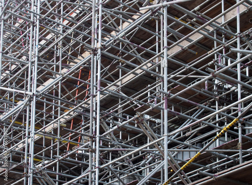 a dense network of metal scaffolding poles supporting work platforms on a construction site