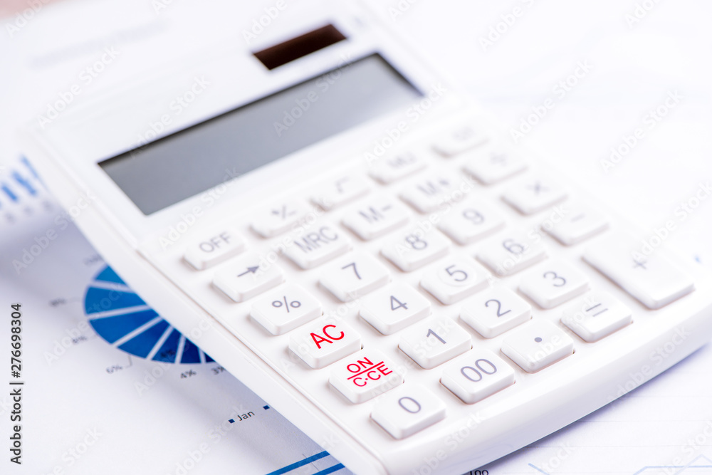 White calculator and report with chart and graph, concept of annual financial profit overview, banking and investment, close up, copy space, macro White calculator and report with chart and graph, concept of annual financial profit overview, banking and investment, close up, copy space, macro