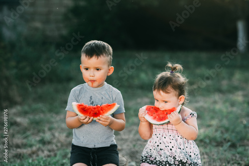 Funny kids eat watermelon. Brother and sister in the open air, sitting on the stumps photo