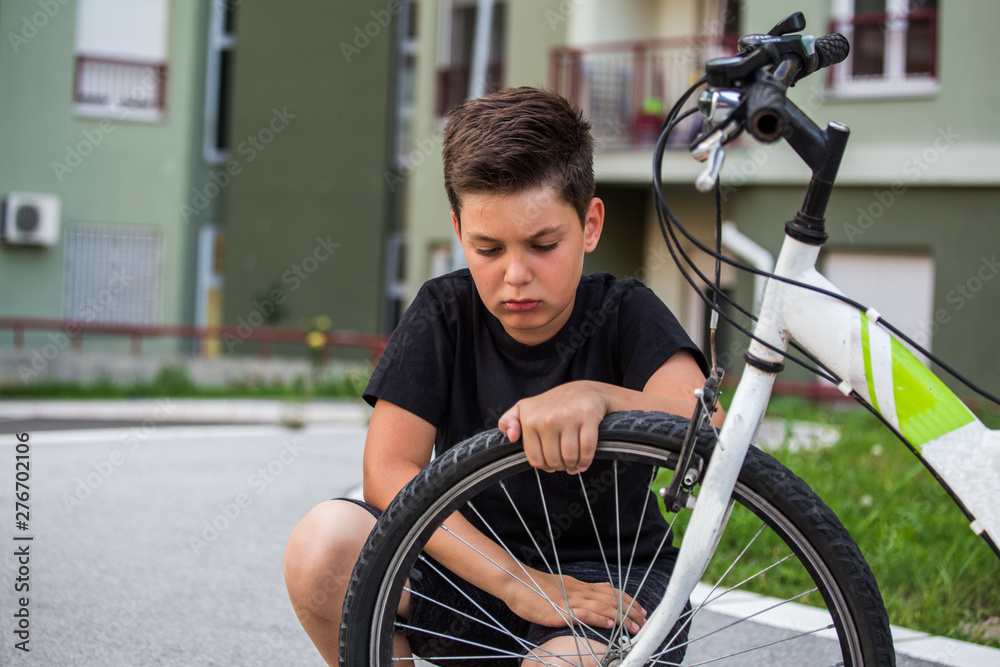 Sad boy looking at his flat bike tire, kid staring at the bicycle with the broken wheel Sad boy looking at his flat bike tire, kid staring at the bicycle with the broken wheel