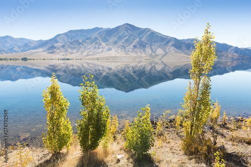 Lake in the dry landscape with trees and mountains. Horizontal image with reflections in the water. Beautiful background photography concept.