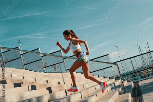 Pushing hard. Full length of beautiful young woman in sports clothing running while exercising outdoors