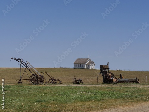 Wide view of vintage farm equipment with a Presbytheran church building in the distance in an 1880s town in South Dakota.  photo