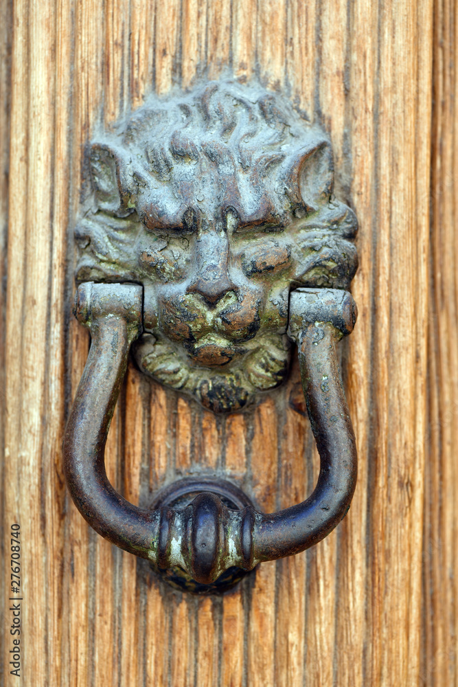 An old door knocker in form of a lion head on an old wooden door in Spain.