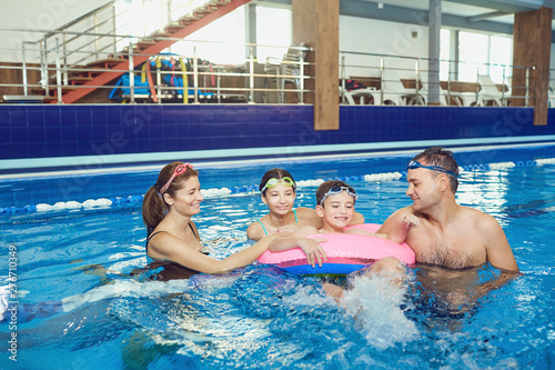 A happy family swims in a swimming pool indoors. 