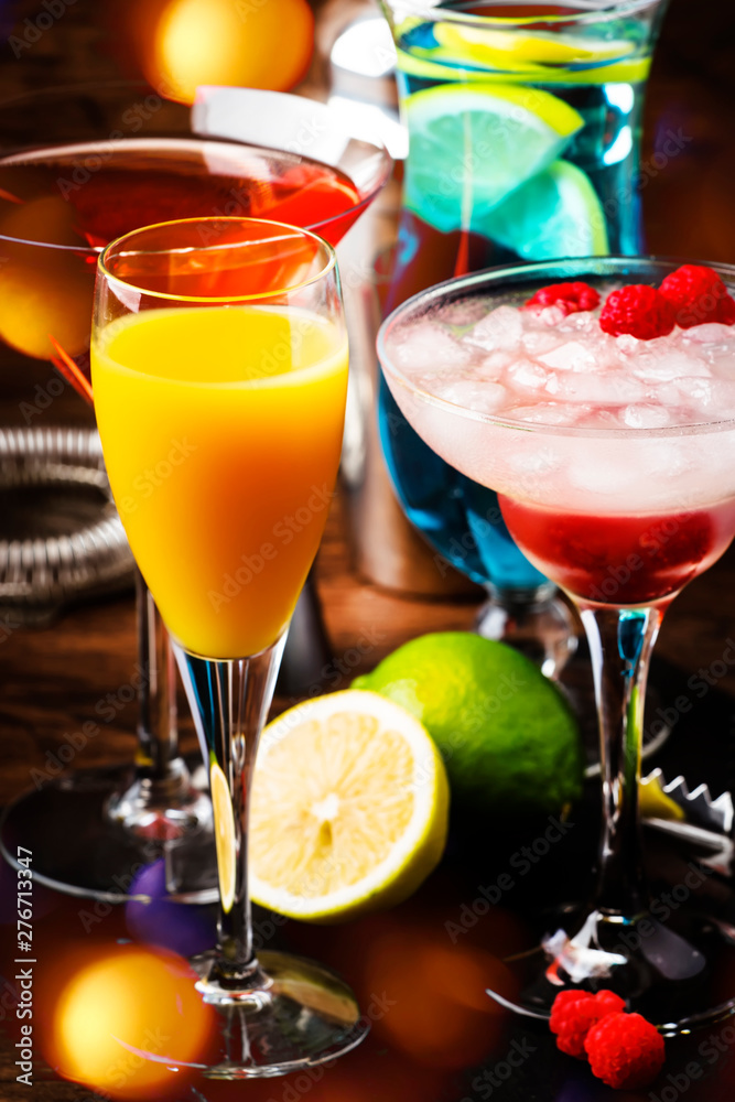 Selection of summer cocktails. Cold refreshing alcoholic beverages and drinks: mimosa, cosmopolitan, raspberry margarita and blue hawaii on wooden bar counter with bar tools