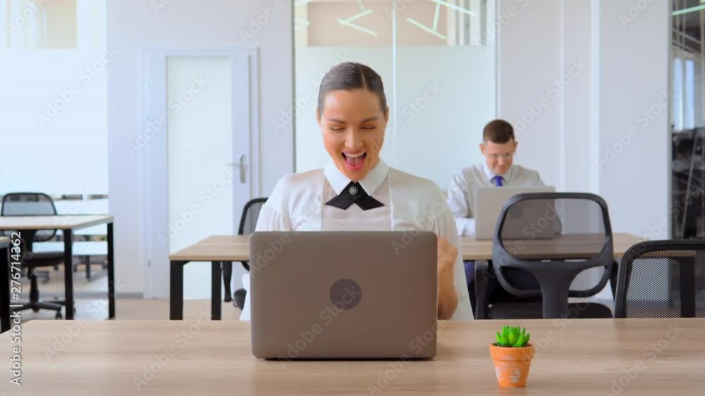Officewoman sitting at table and her eyes are on computer. Suddenly she exclaims her joy with a gesture and facial movements Near there is a green plant and another man sits behid her Officewoman sitting at table and her eyes are on computer. Suddenly she exclaims her joy with a gesture and facial movements Near there is a green plant and another man sits behid her