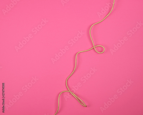 twisted golden cable in a textile winding on a pink background