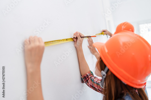 young asian women with yellow tape measure and pencil is measuring the area inside the white room selective focus