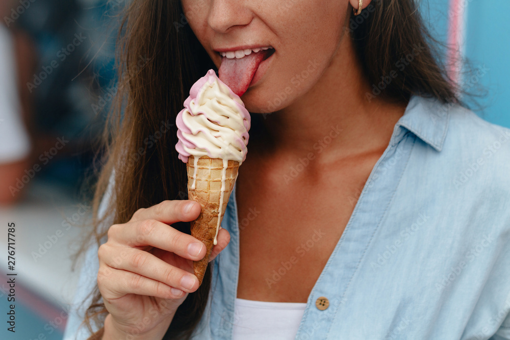 Young woman eating sweet ice cream cone in summer hot weather in street