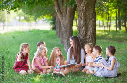 children hold a lesson with the teacher in the park on a green lawn.