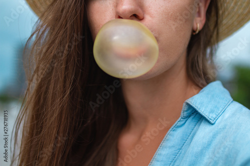 Hipster woman in hat blowing bubble of chewing gum outdoor