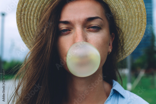 Quadro su tela Young attractive woman in hat blowing bubble of chewing gum outdoor