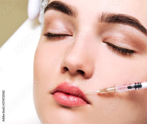 The doctor cosmetologist beautician makes the rejuvenating facial botox injections procedure for tightening and smoothing wrinkles on the face skin to lips of a beautiful young woman in a beauty salon