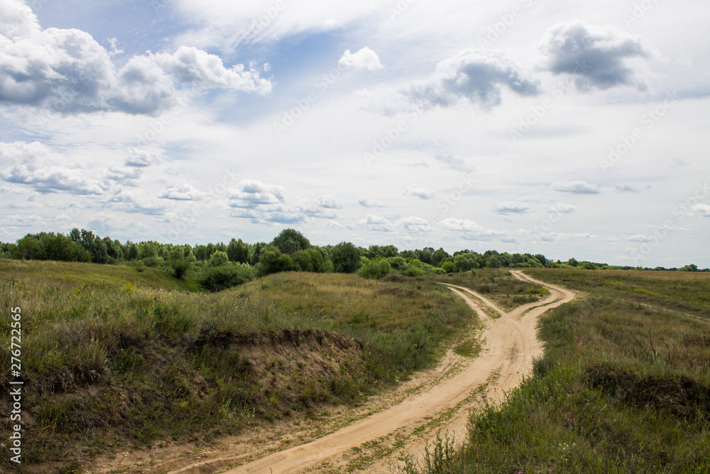 Country road in a field with grass and hills on a clear summer day Country road in a field with grass and hills on a clear summer day