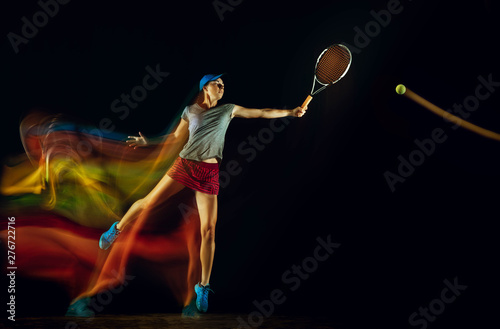 One caucasian woman playing tennis isolated on black background in mixed and stobe light. Fit young female player in motion or action during sport game. Concept of movement, sport, healthy lifestyle. © master1305