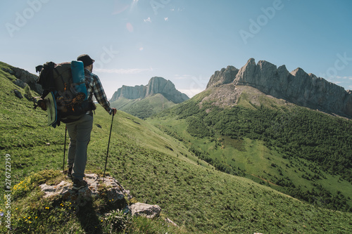  young guy with a tourist backpack looks at the mountain peaks on a sunny summer day