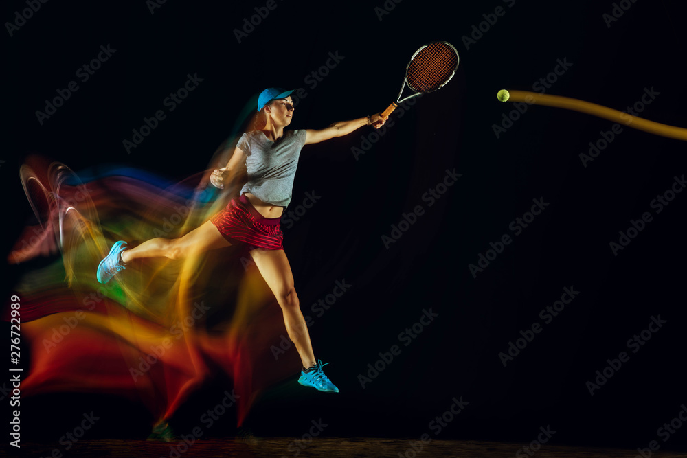 Fototapeta premium One caucasian woman playing tennis isolated on black background in mixed and stobe light. Fit young female player in motion or action during sport game. Concept of movement, sport, healthy lifestyle.