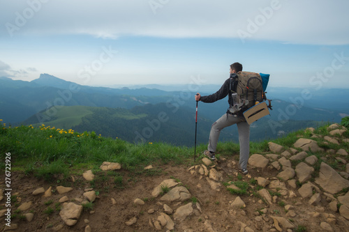  young guy with a tourist backpack looks at the mountain peaks on a sunny summer day