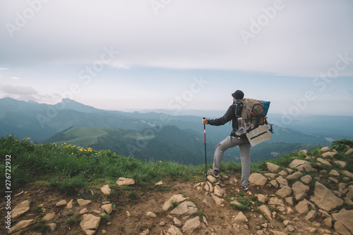  young guy with a tourist backpack looks at the mountain peaks on a sunny summer day