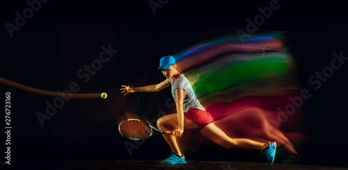 One caucasian woman playing tennis isolated on black background in mixed and stobe light. Fit young female player in motion or action during sport game. Concept of movement, sport, healthy lifestyle.