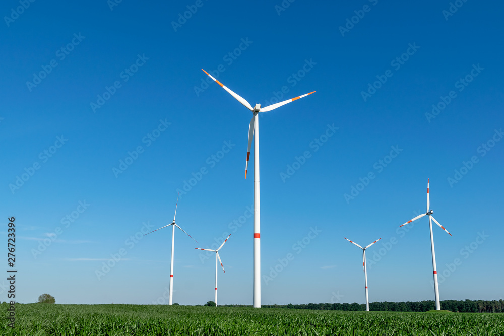 Low angle view of five wind power turbines, part of a wind farm, on a green field in eastern Germany near the city of Cottbus, Brandenburg. Wind turbines are part of the energy transition strategy. Low angle view of five wind power turbines, part of a wind farm, on a green field in eastern Germany near the city of Cottbus, Brandenburg. Wind turbines are part of the energy transition strategy.