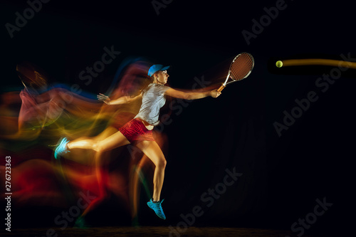 One caucasian woman playing tennis isolated on black background in mixed and stobe light. Fit young female player in motion or action during sport game. Concept of movement, sport, healthy lifestyle. © master1305