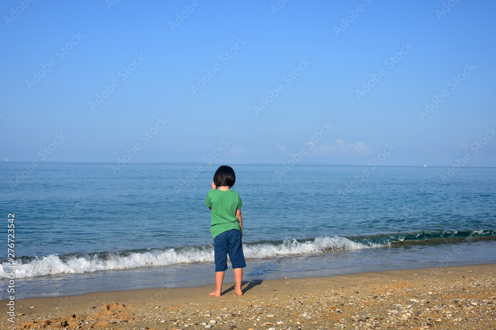 Child play at sea coast. Little boy at the beach, Child look a waves in the sea