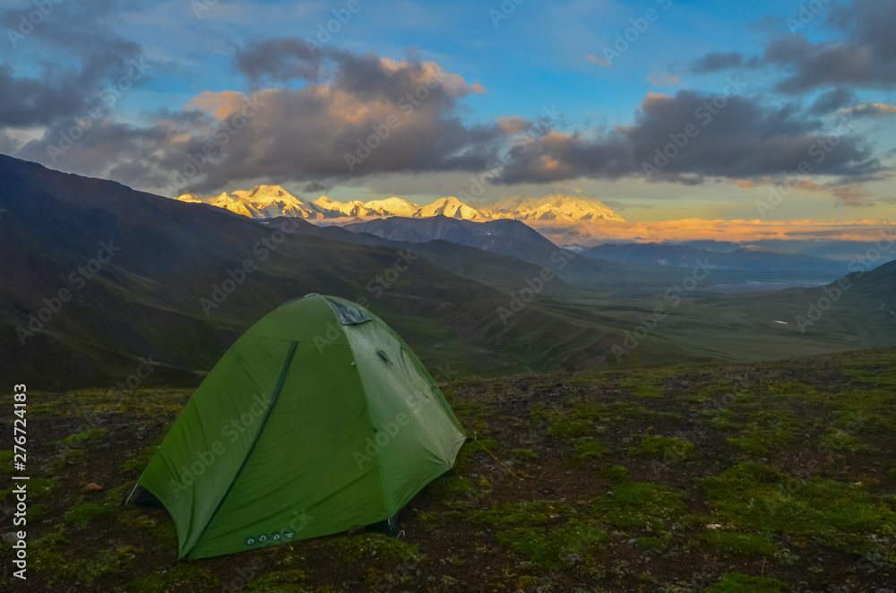 Sunrise view of Mount Denali - mt Mckinley peak with alpenglow during golden hour with green camping tent in the foreground from Stony Dome overlook.