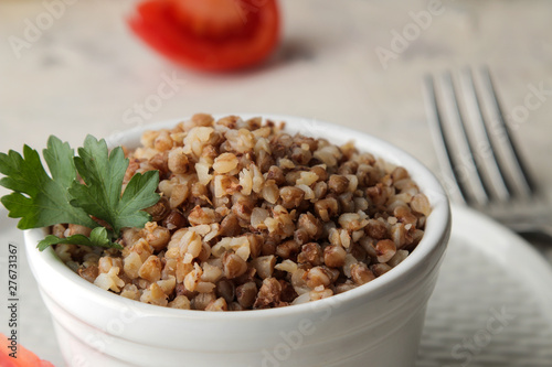 Buckwheat. Porridge cereals with parsley in a white ceramic bowl and tomato on a bright table. breakfast, healthy food.