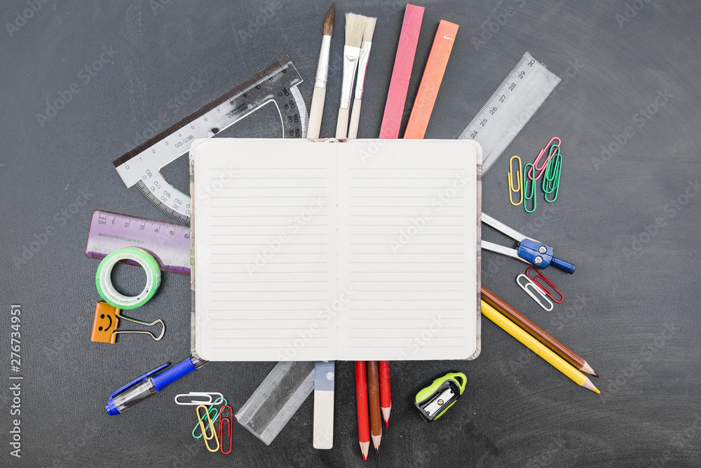 Notebook with stationery on blackboard Notebook with stationery on blackboard