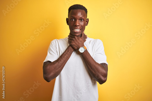 Young african american man wearing white t-shirt standing over isolated yellow background shouting and suffocate because painful strangle. Health problem. Asphyxiate and suicide concept.