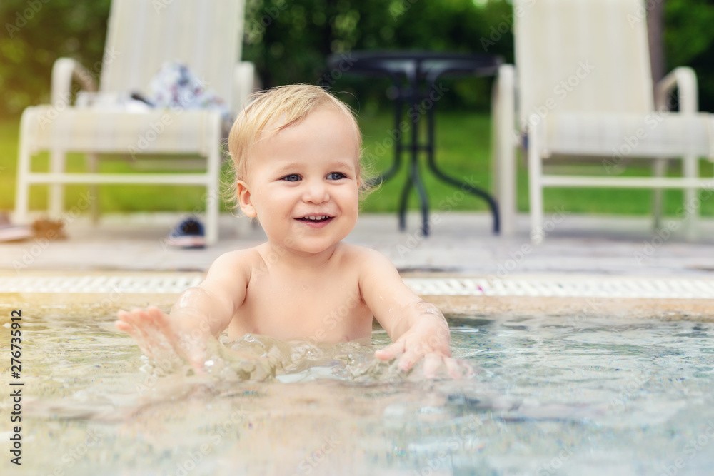 Happy little caucasian blond toddler boy swimming in wading pool on bright summer day at resort. Adorable baby enjoying outdoor water fun activities in shallow water. Children travel and holidays Happy little caucasian blond toddler boy swimming in wading pool on bright summer day at resort. Adorable baby enjoying outdoor water fun activities in shallow water. Children travel and holidays