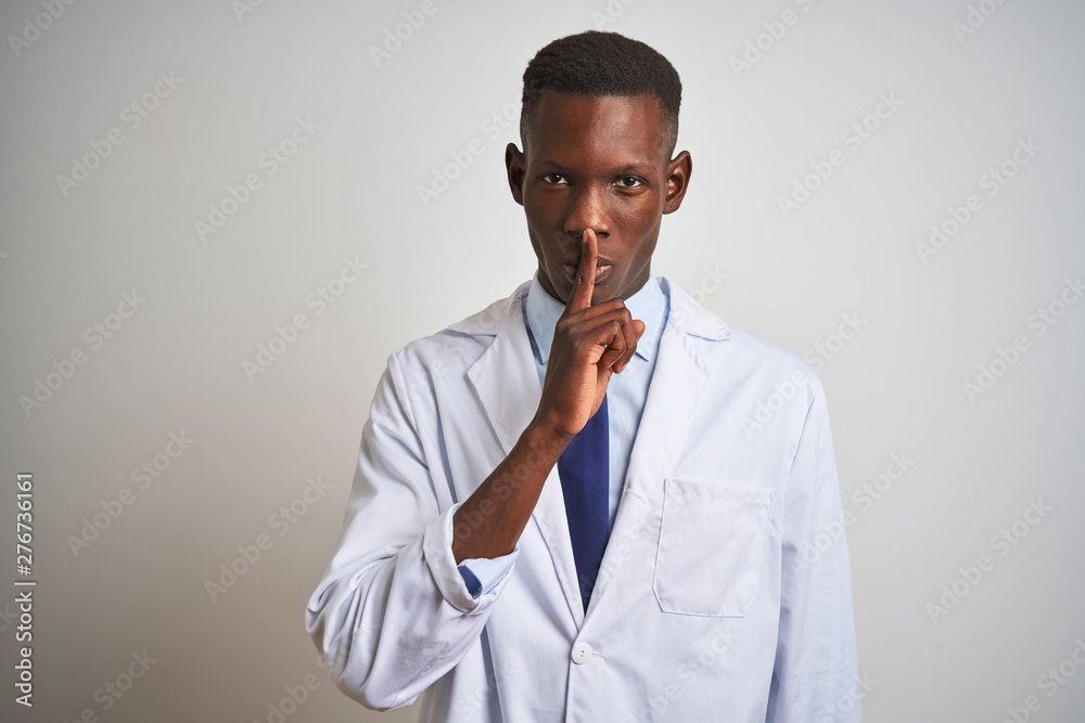 Young african american doctor man wearing coat standing over isolated white background asking to be quiet with finger on lips. Silence and secret concept. Young african american doctor man wearing coat standing over isolated white background asking to be quiet with finger on lips. Silence and secret concept.