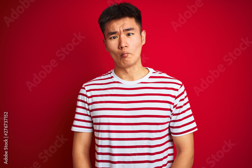 Wallpaper Mural Young asian chinese man wearing striped t-shirt standing over isolated red background making fish face with lips, crazy and comical gesture. Funny expression. Torontodigital.ca