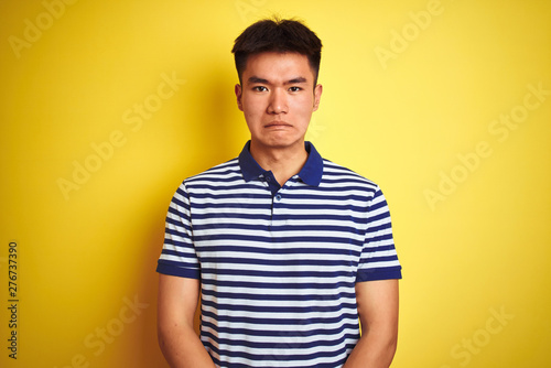 Young asian chinese man wearing striped polo standing over isolated yellow background depressed and worry for distress  crying angry and afraid. Sad expression.