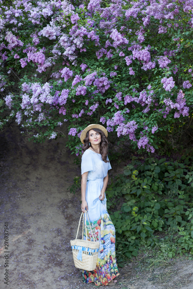 Beautiful girl enjoying the smell of lilac on a summer day. Aromatherapy and spring concept. A pretty girl, a beautiful woman in a blue long vintage dress is standing in a lilac garden. Gardening Beautiful girl enjoying the smell of lilac on a summer day. Aromatherapy and spring concept. A pretty girl, a beautiful woman in a blue long vintage dress is standing in a lilac garden. Gardening