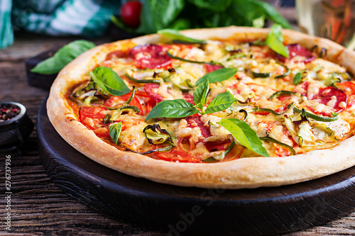 Italian pizza with chicken, salami, zucchini, tomatoes and herbs on vintage wooden background. Italian cuisine