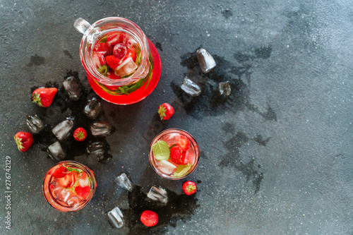Glasses and Carafe with Organic Strawberry Drink. Refrigerated Refreshing Mixed Ripe Berries and Mint Green Leaves in Vitamin Bio Liquid. Splash of Water and Ice. Sweet Delicious Beverage Top View